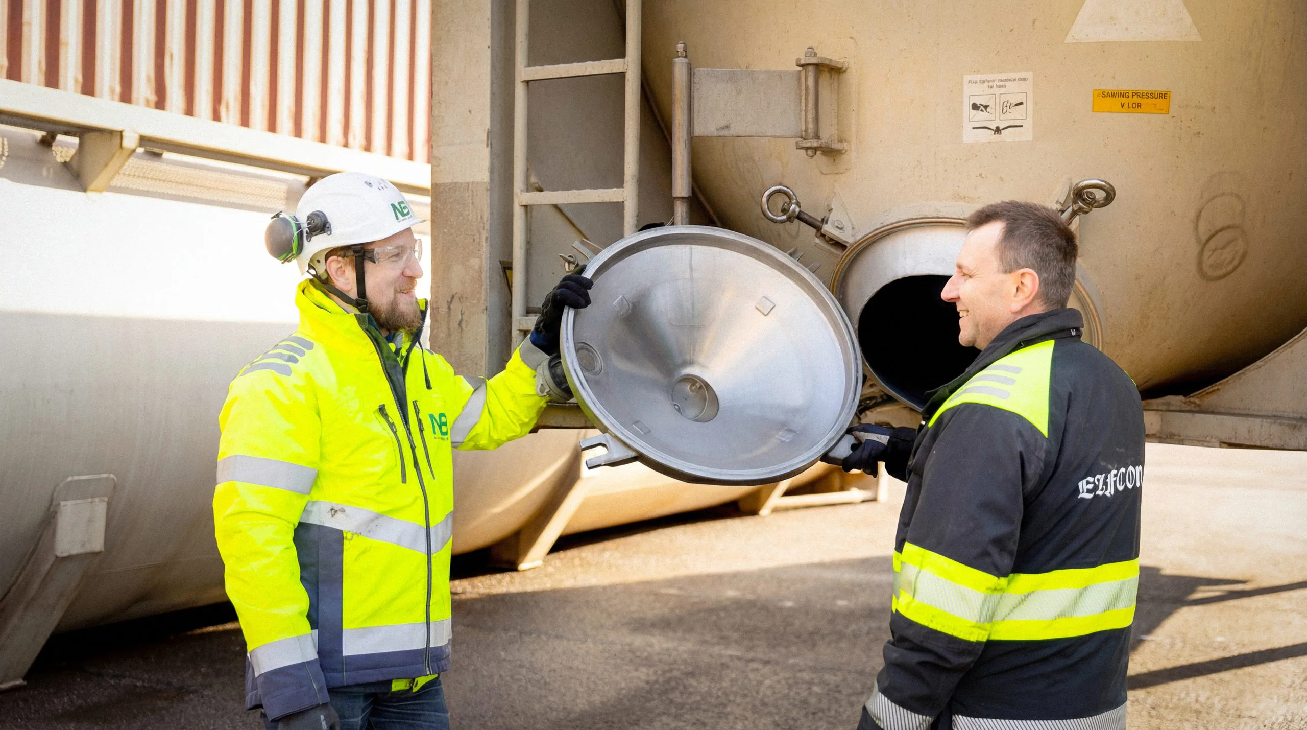 Två tekniker inspekterar en öppen lucka på en tankcontainer.