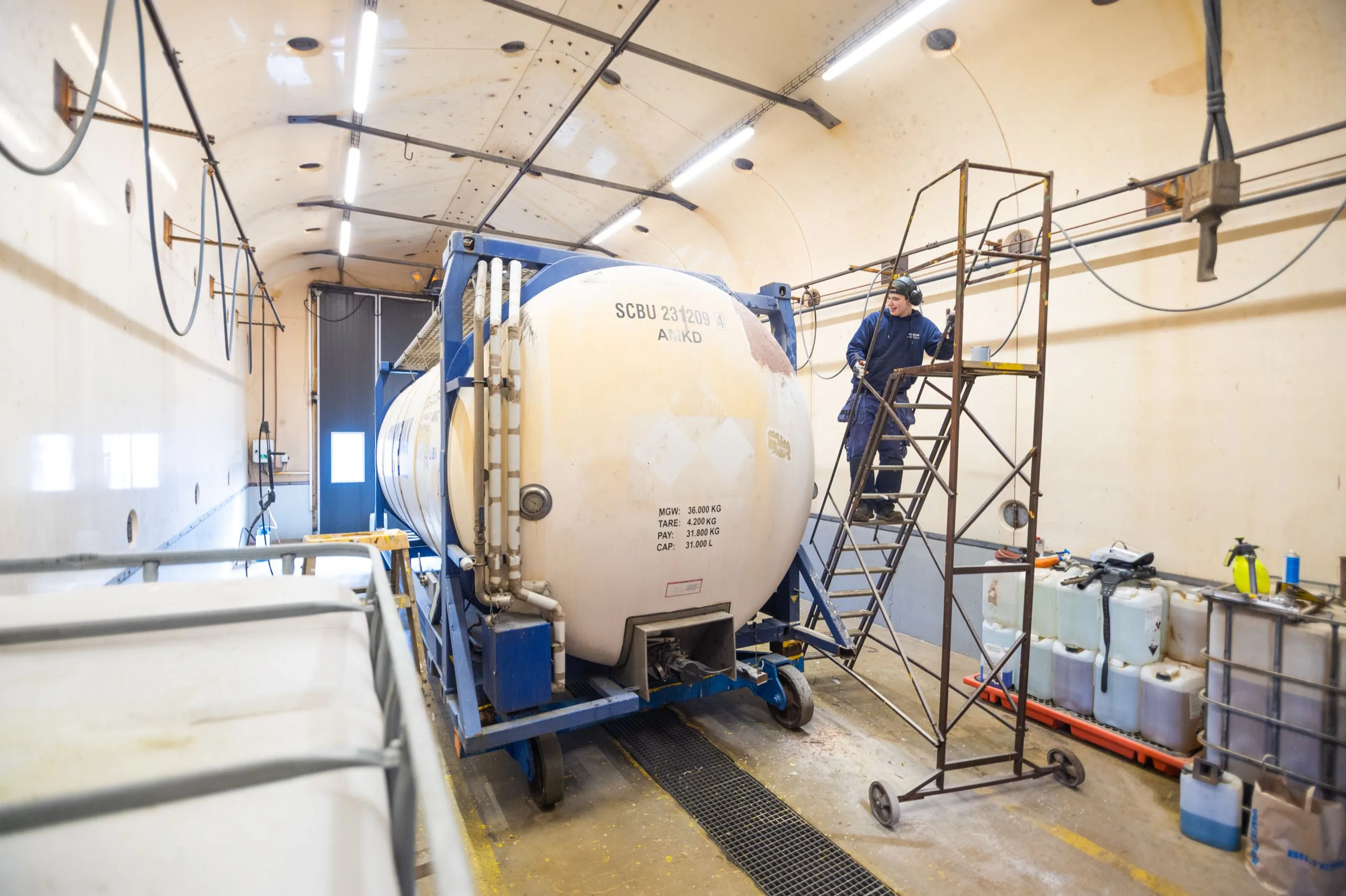 En tekniker servar en vit tankcontainer från en arbetsplattform.